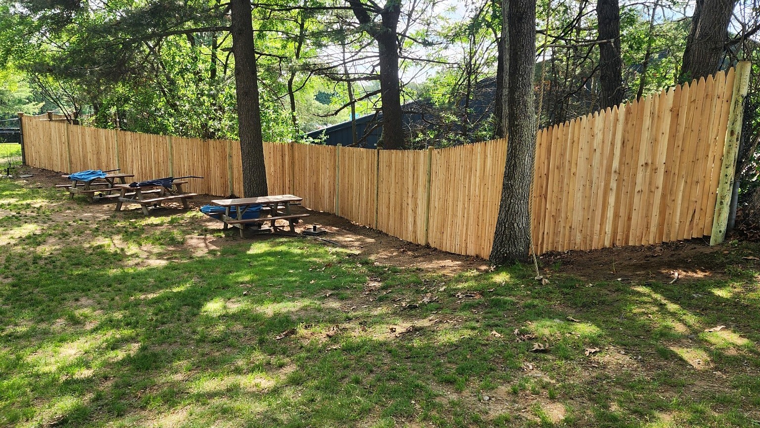 Cedar fence run with a taller right-hand section at a wooded property.