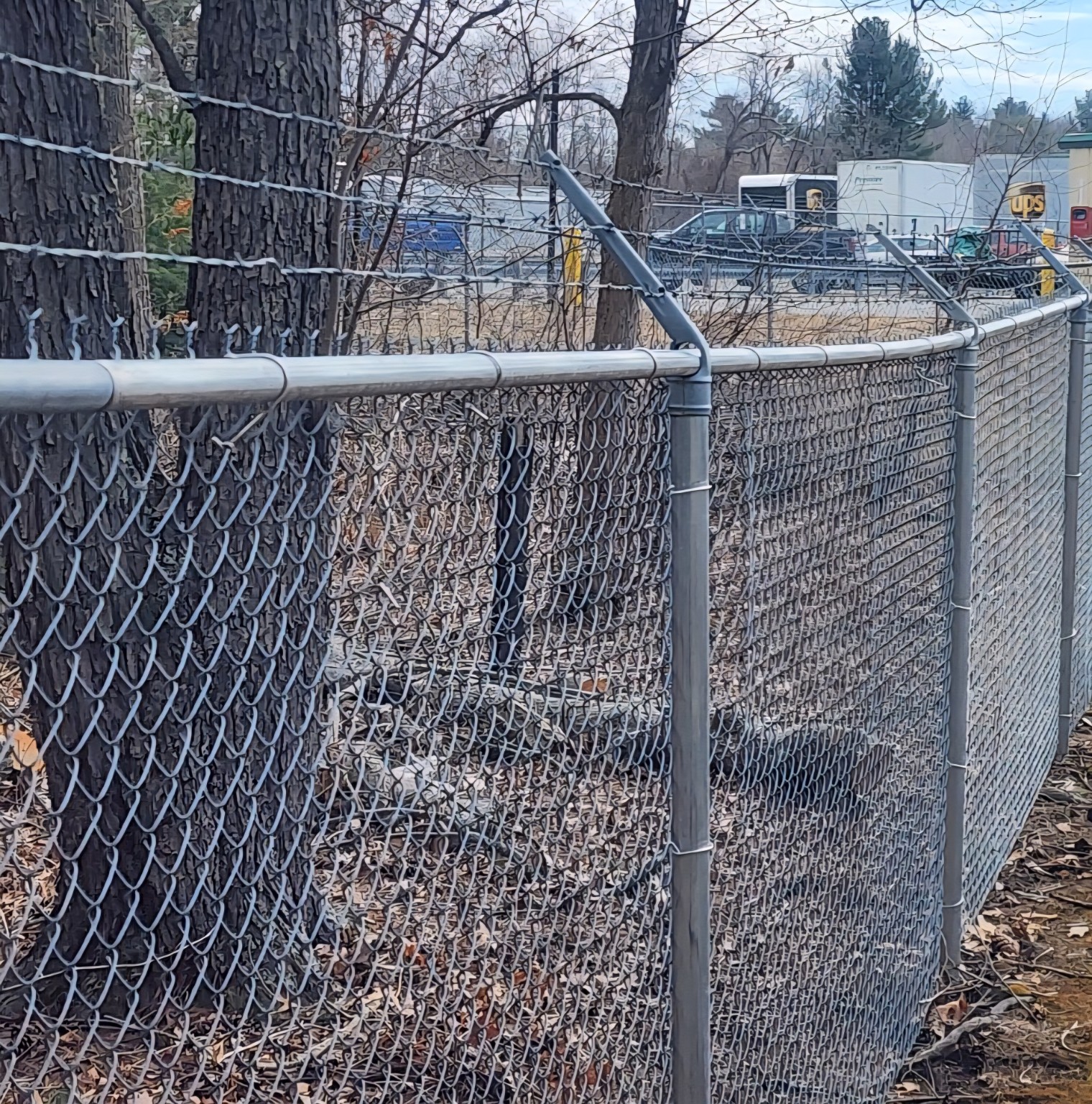 Galvanized chain-link security fence with angled barbed-wire arms beside a vehicle lot.
