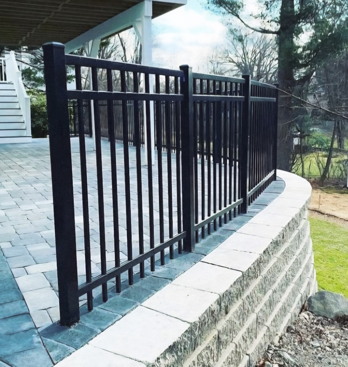 Black metal railing along a curved stone retaining wall beside a paved patio and house.